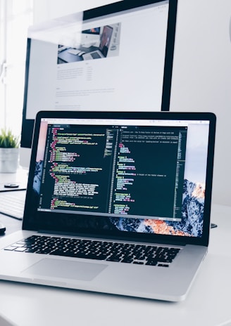 A MacBook with lines of code on its screen on a busy desk